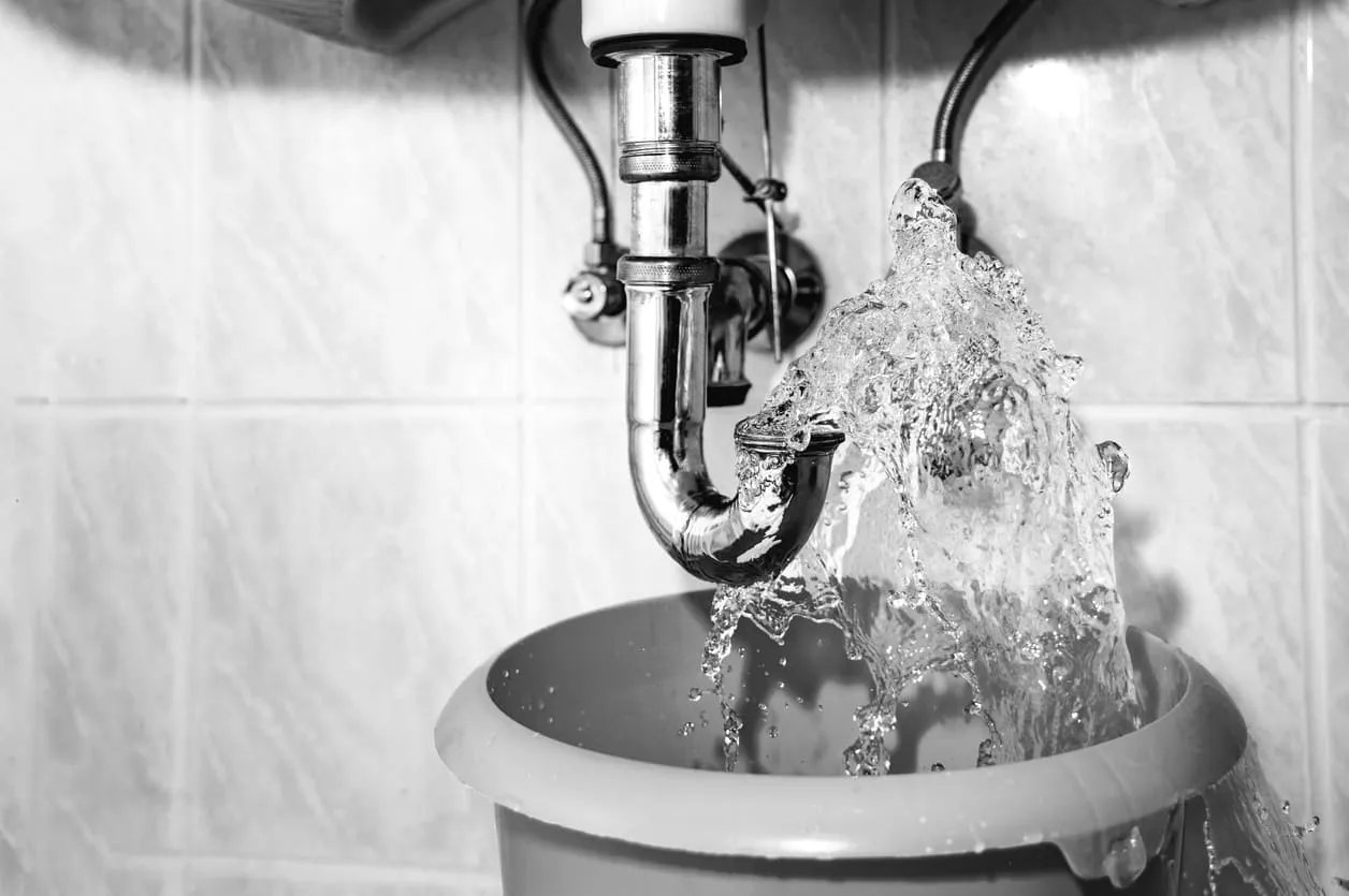 Water gushing from a burst pipe under a sink into a bucket